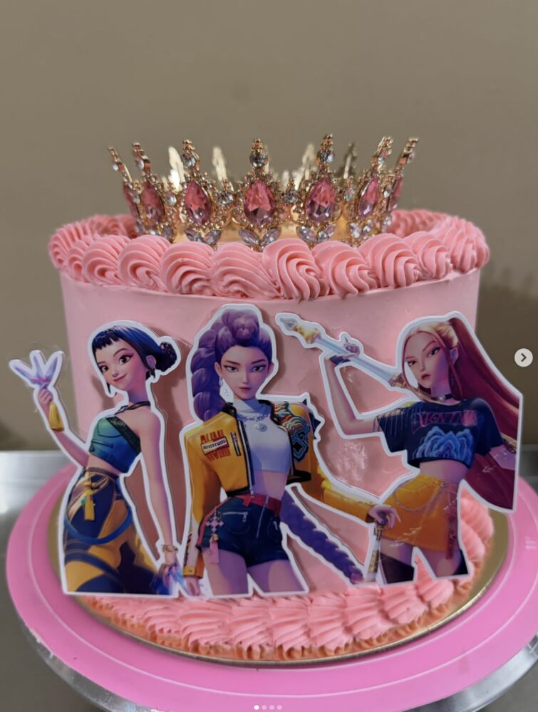 Pink cake with custom printed character cutouts and a jeweled crown topper